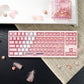 Pink and white keyboard on a desk with decorative items