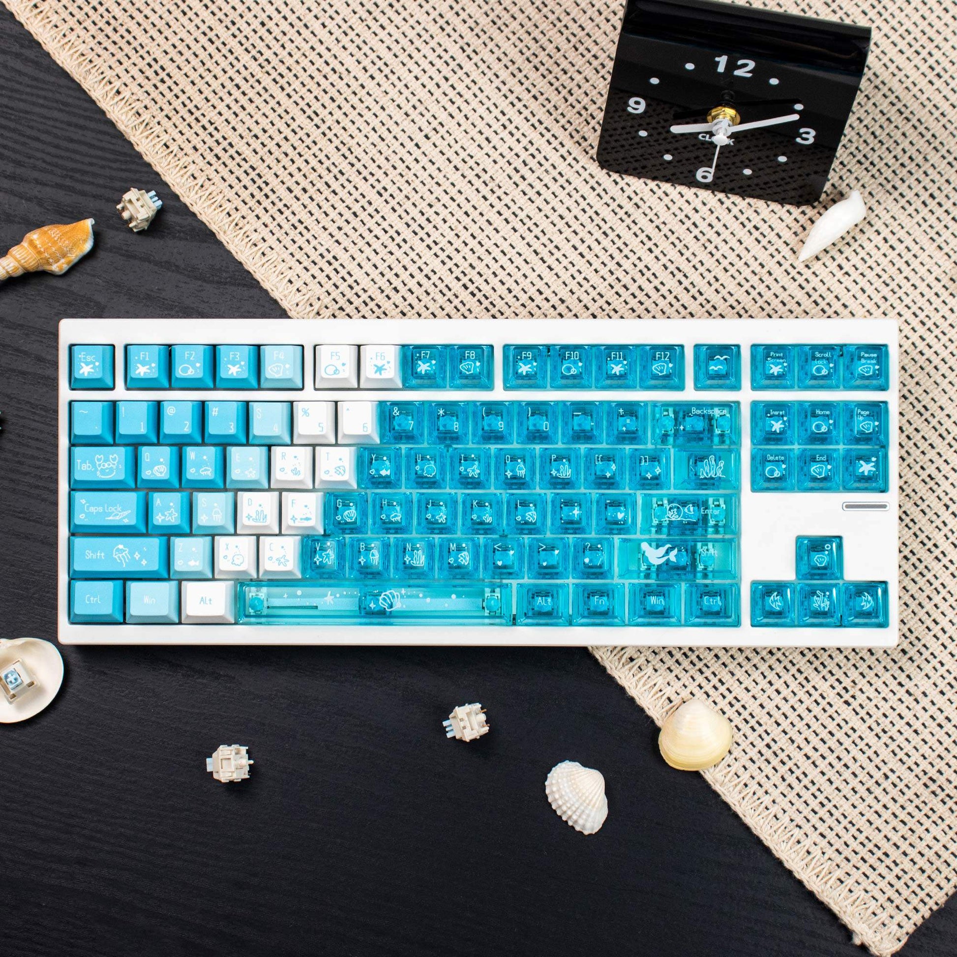Keyboard with blue and white keys on a textured surface with shells and a clock.